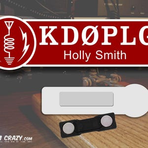 May include: A red and white name tag with the call sign "KD&Oslash;PLG" and the name "Holly Smith" printed on it. The tag is next to a white name tag with a magnetic backing.