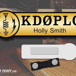 May include: A gold name tag with the call sign "KD&Oslash;PLG" and the name "Holly Smith" printed in black text. The tag is attached to a white magnetic name tag holder with a black magnetic clasp.