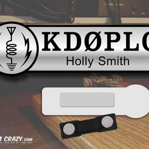 May include: A silver name tag with a black and white logo of an antenna and the call sign "KD&Oslash;PLG" and the name "Holly Smith" printed below.