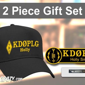 May include: A black baseball cap and a name tag with the text "KDØPLG Holly Smith". The cap and name tag have a yellow and black design with a radio wave symbol. The gift set is a 2-piece set.