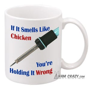 May include: White ceramic mug with a blue and black soldering iron graphic. The text on the mug reads "If It Smells Like Chicken You're Holding It Wrong".