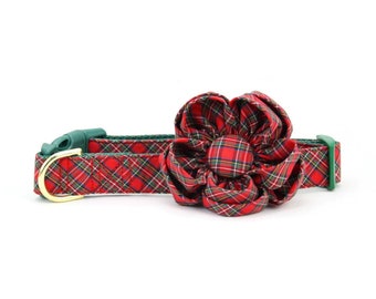May include: A red and green plaid dog collar with a matching flower accessory. The collar has a green buckle and a gold-colored metal clasp. The flower is made of the same plaid fabric.