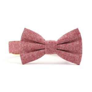 May include: A red bow tie made of a textured fabric. The bow tie is attached to a brown collar.