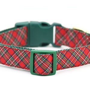 May include: A pet collar featuring a red, green, yellow, and white plaid pattern on fabric. The collar includes a dark green plastic side-release buckle and a matching dark green plastic adjustable slider for securing the fit around the neck.