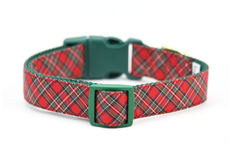 May include: A pet collar featuring a red, green, yellow, and white plaid pattern on fabric. The collar includes a dark green plastic side-release buckle and a matching dark green plastic adjustable slider for securing the fit around the neck.