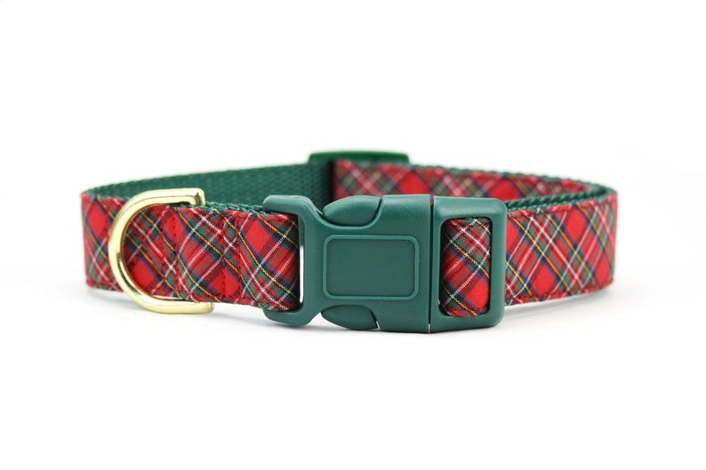 May include: A pet collar featuring a red, green, and yellow plaid fabric pattern. The collar includes a dark green plastic side-release buckle and a gold-toned metal D-ring for attachment. The inner lining of the collar is a solid dark green.