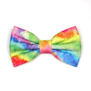 May include: A rainbow tie dye bow tie with a watercolor pattern. The bow tie is made of fabric and has a bright, colorful design.