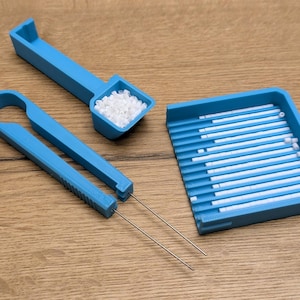 Könnte beinhalten: Ein blaues Plastikwerkzeug zum Organisieren und Sortieren von kleinen Perlen. Das Werkzeug enthält eine Schaufel, eine Pinzette und eine Schale mit Reihen von kleinen Fächern.