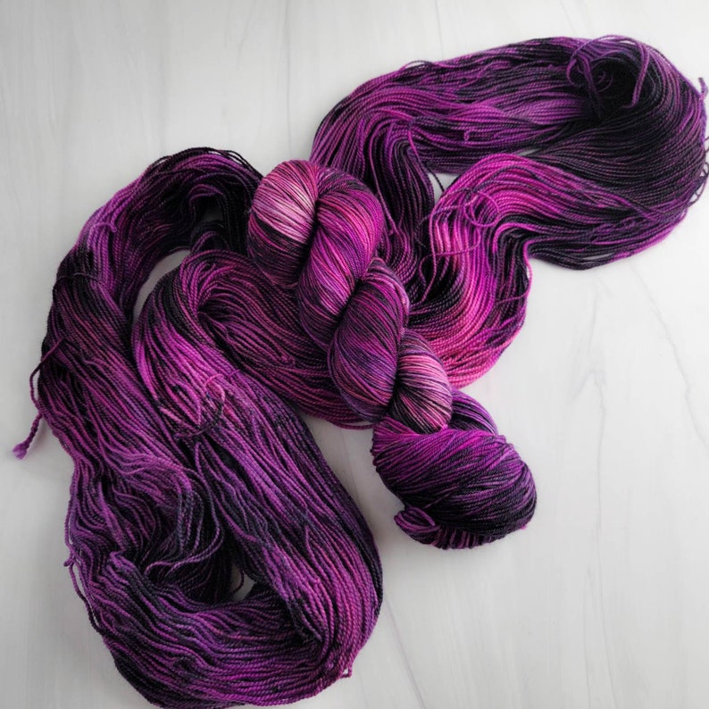 May include: A skein of purple and black yarn with a gradient effect. The yarn is soft and fluffy, and it would be perfect for knitting or crocheting.