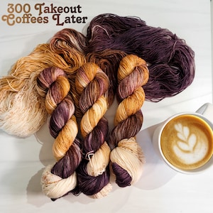 May include: Three skeins of yarn in shades of brown, cream, and purple. The yarn is arranged in a spiral pattern. The text "300 Takeout Coffees Later" is visible in the top left corner of the image. A cup of coffee with latte art is visible in the bottom right corner of the image.