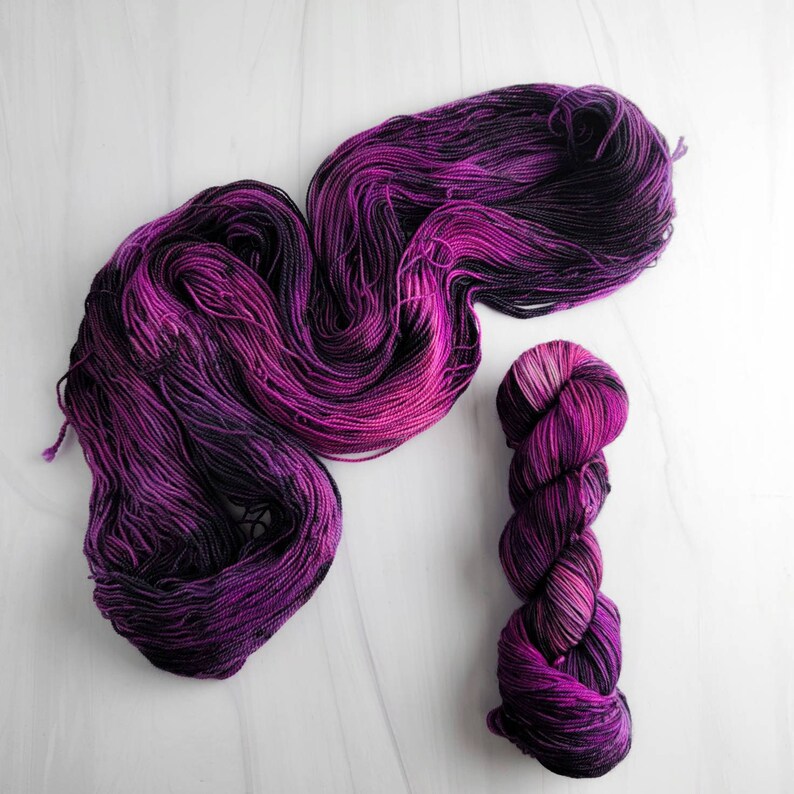 May include: A skein of purple and black yarn with a smaller skein of the same yarn wound into a ball.