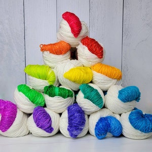 May include: A stack of white yarn balls with colorful stripes of yarn inside. The yarn balls are arranged in a pyramid shape.