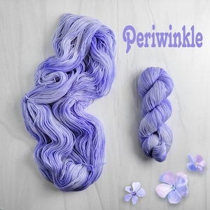 May include: A skein of periwinkle blue yarn with white highlights. The yarn is arranged in a loose coil and a smaller coil. The word "Periwinkle" is written in purple letters above the yarn.