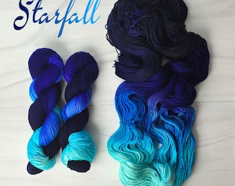 Può includere: Due gomitoli di filato sfumato blu e turchese con la parola "Starfall" scritta in corsivo sopra.