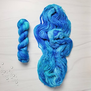 May include: Two skeins of blue and turquoise yarn, one skein is twisted into a rope shape, the other is loose and spread out.