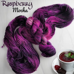 May include: A skein of purple and black yarn with the text "Raspberry Mocha" on a white background.