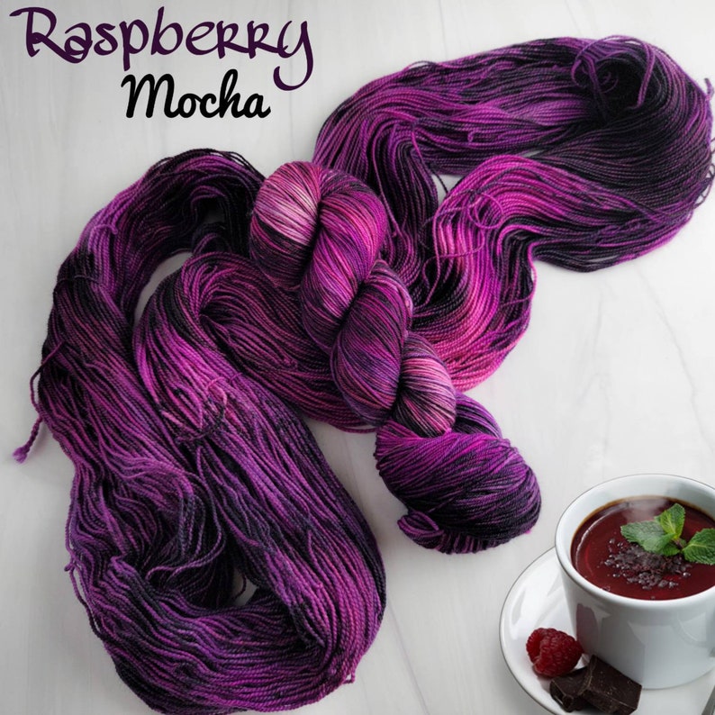 May include: A skein of purple and black yarn with the text "Raspberry Mocha" on a white background.