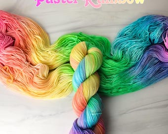 May include: Pastel Rainbow yarn in shades of pink, yellow, green, and blue. The yarn is arranged in a rainbow pattern and is ready to be used for knitting or crocheting.