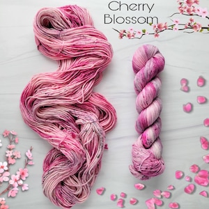 May include: Two skeins of pink and white yarn with a speckled pattern. The yarn is called "Cherry Blossom".