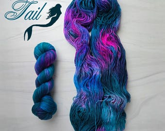Puede incluir: Dos madejas de hilo teñido a mano en tonos turquesa, azul, morado y rosa. Una madeja está enrollada, la otra suelta. El texto "Mermaid Tail" está en la esquina superior izquierda, con una silueta de sirena.