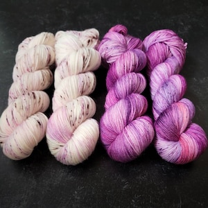 May include: Four skeins of yarn in shades of pink and white. The yarn is hand-dyed and has a speckled appearance.