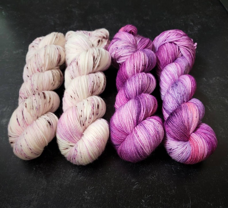 May include: Four skeins of yarn in shades of pink and white. The yarn is hand-dyed and has a speckled appearance.
