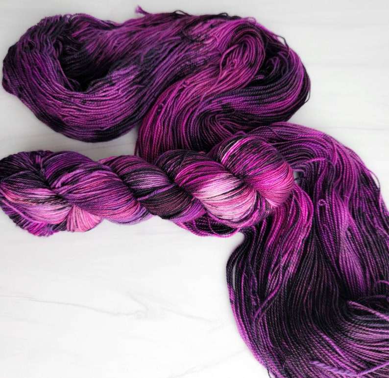 May include: A skein of purple and black yarn with a gradient of colour. The yarn is soft and fluffy, and it would be perfect for knitting or crocheting.