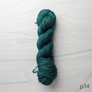 May include: A skein of teal-colored yarn, tightly twisted and ready for knitting or crocheting. The yarn has a slight sheen, and the color varies slightly throughout the skein. The background is a white marble-like surface. The text "p14" is in the bottom right corner.