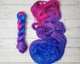 May include: A skein of yarn in a pink, purple, and blue ombre colorway. The yarn is wound into a ball and is ready to be used for knitting or crocheting.