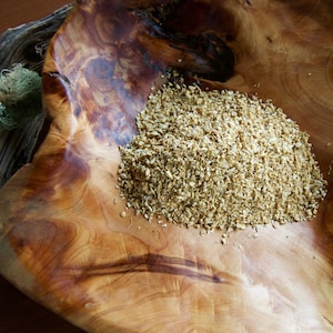Könnte beinhalten: Eine Holzschale mit natürlicher, warmer Holzmaserung, gefüllt mit einem Haufen hellbraunen, körnigen Materials. Die Schale steht auf einer dunklen Holzoberfläche, mit einem Stück Treibholz und Moos im Hintergrund.