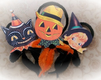 May include: Three vintage Halloween decorations made of paper and pipe cleaners. A black cat with a pointed hat, a jack-o-lantern with a yellow hat, and a girl with a witch's hat.