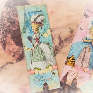 May include: Two vintage-style bookmarks with a Parisian theme. Each bookmark features a woman in a dress, a butterfly, and the text "Paris". One bookmark is pink and blue with the text "Marie Antoinette 1775". The other bookmark is blue and green with the text "Marie Antoinette 1775".