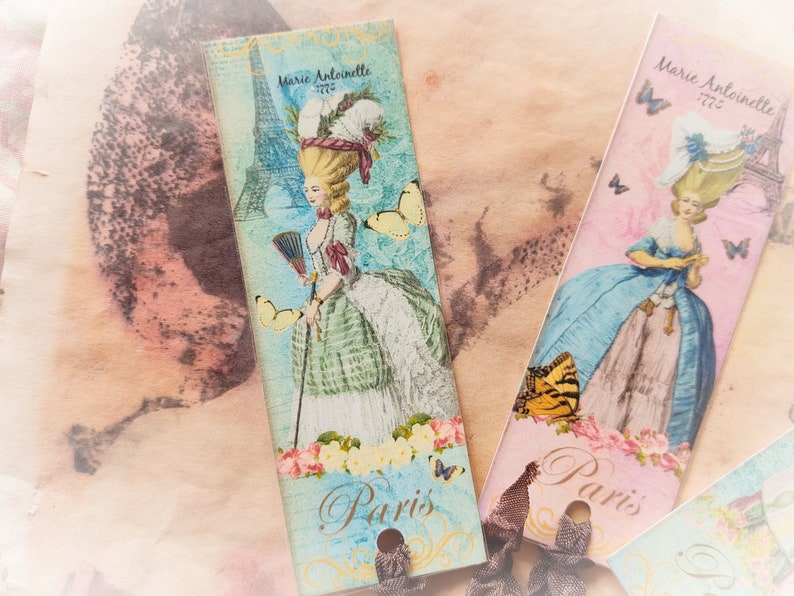 May include: Two vintage-style bookmarks with a Parisian theme. Each bookmark features a woman in a dress, a butterfly, and the text "Paris". One bookmark is pink and blue with the text "Marie Antoinette 1775". The other bookmark is blue and green with the text "Marie Antoinette 1775".