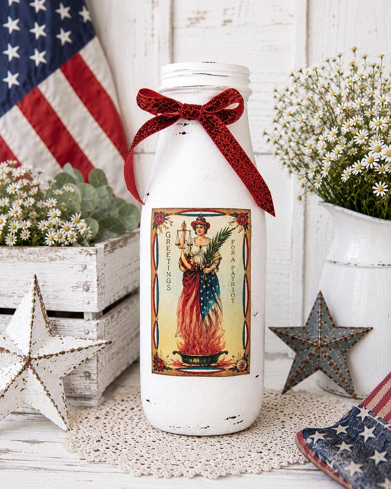 May include: A white painted glass bottle with a red glitter bow and a vintage patriotic label. The label features a woman in a dress with the American flag design. The bottle is decorated with a red glitter bow and is surrounded by patriotic decor.
