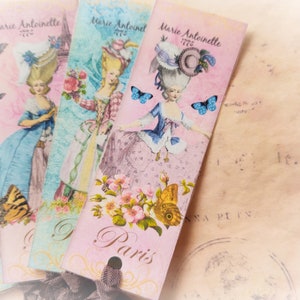 May include: Four pink, blue, and green bookmarks with a vintage design featuring a woman in a white dress and a blue hat. The bookmarks have the text "Marie Antoinette 1776" and "Paris" printed on them.