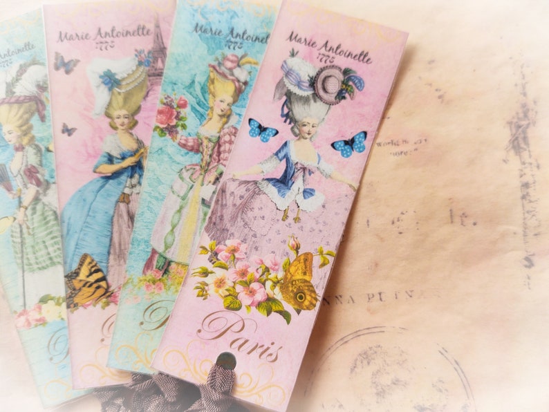 May include: Four pink, blue, and green bookmarks with a vintage design featuring a woman in a white dress and a blue hat. The bookmarks have the text "Marie Antoinette 1776" and "Paris" printed on them.
