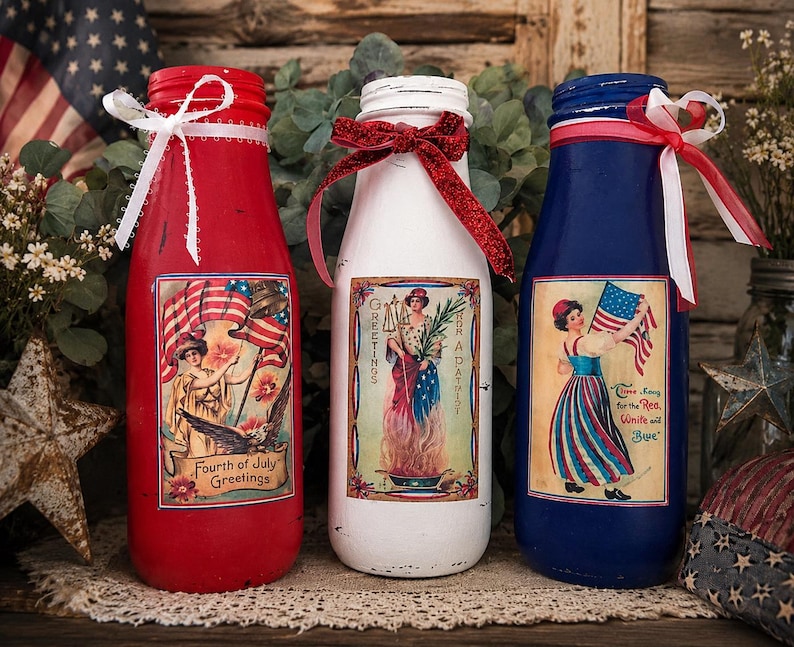 May include: Three painted glass bottles in red, white, and blue, decorated for the Fourth of July. Each bottle features a vintage-style patriotic image and is adorned with ribbons and lace. The red bottle has the text "Fourth of July Greetings".
