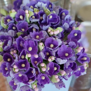 May include: A bouquet of purple paper flowers with pink centers. The flowers are arranged in a cluster and have a soft, velvety texture.