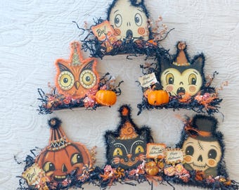 May include: A collection of six Halloween-themed wooden cutouts featuring a ghost, owl, cat, pumpkin, and skull. Each piece is decorated with black tinsel, small orange pumpkins, and signs with text including Boo and Happy Halloween.