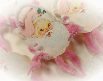 May include: Pink and white Christmas ornaments featuring a cartoon Santa Claus with a white beard and a pink hat. The ornaments are attached to pink pipe cleaners.