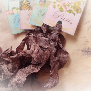 May include: A pile of brown ruffled ribbon with vintage style tags that say "Paris" and "London" on them.