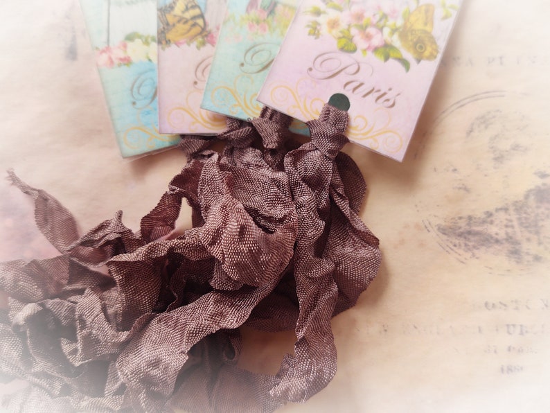 May include: A pile of brown ruffled ribbon with vintage style tags that say "Paris" and "London" on them.