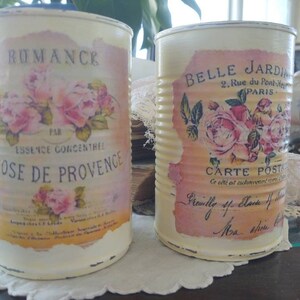 Op de afbeelding: Twee vintage-stijl metalen blikken met bloemmotieven en Franse tekst. De blik aan de linkerkant zegt "Romance" en "Rose de Provence". De blik aan de rechterkant zegt "Belle Jardin" en "Carte Postale".