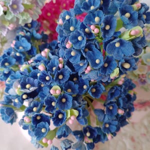 May include: A bouquet of blue felt flowers with pink centers. The flowers are arranged in a cluster and have a delicate, vintage aesthetic.