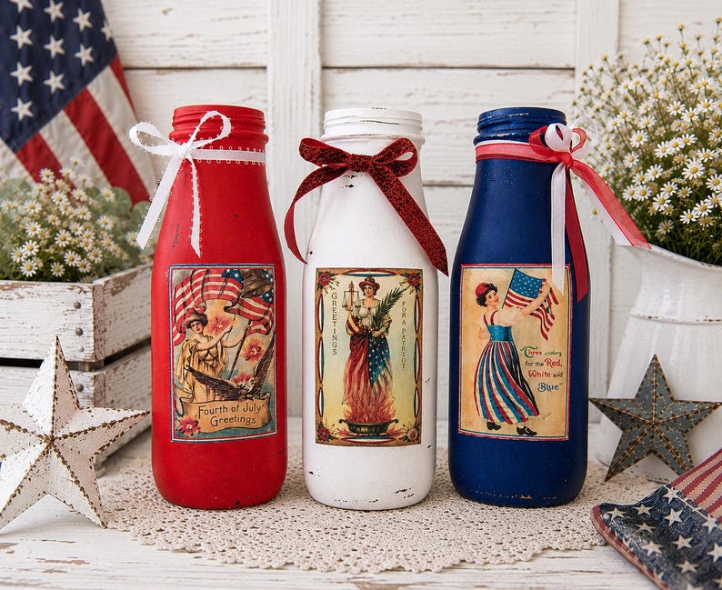 May include: Three decorative glass bottles painted red, white, and blue, with patriotic labels and ribbon accents. The bottles are decorated with vintage-style images and text, perfect for Fourth of July celebrations.