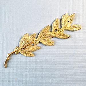 May include: A gold-coloured metal leaf garland with a textured surface. The garland is made of several leaves connected together by a stem.