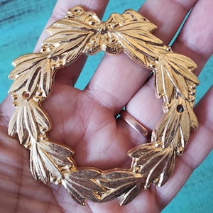 Peut inclure: Une couronne en métal doré avec un nœud au centre. La couronne est faite de feuilles et a une finition lisse et brillante.