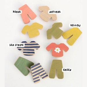 May include: Wooden clothing shapes in various colors, including yellow, green, blue, and red. The shapes are labeled with the colors: "Koral", "Natural", "Yellow", "Sea Stripe", "Green".