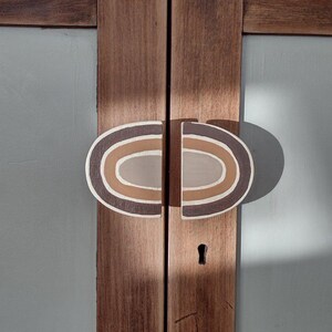 Op de afbeelding: Een paar bruine houten kastdeuren met een unieke ovale deurknop. De deurknop is geschilderd met concentrische cirkels in tinten bruin, beige en wit.