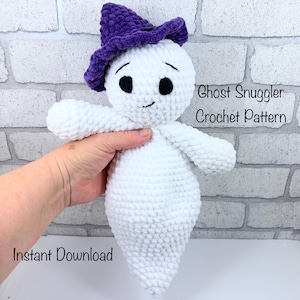 May include: A white crocheted ghost doll wearing a purple hat. The ghost has black eyes and a small smile. The text "Ghost Snuggler Crochet Pattern" and "Instant Download" are visible.